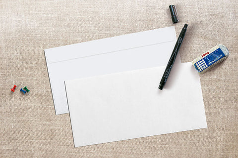 white linen envelopes on desk with pen and eraser